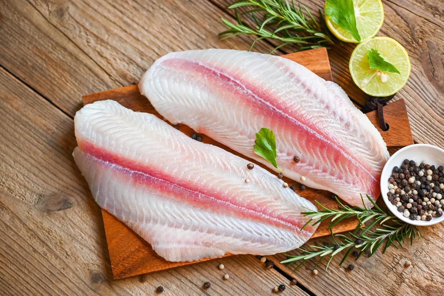 fish fillet on wooden board with ingredients for cooking, meat dolly fish tilapia striped catfish, fresh raw pangasius fish fillet with herb and spices black pepper lemon lime - top view photo