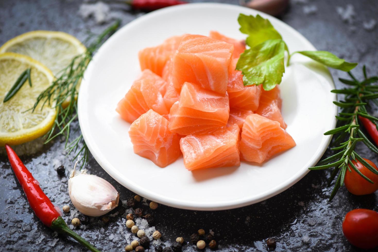 Raw salmon filet cube with herbs and spices on white plate dark  background Fresh salmon fish for cooking salad seafood pepper rosemary lemon pepper photo