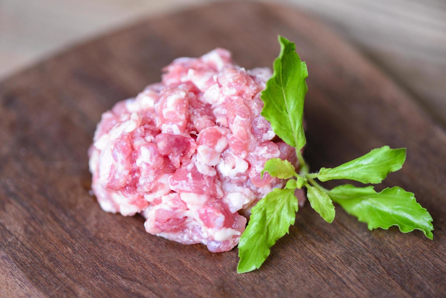 carne picada, carne picada o molida - cerdo crudo con hoja de albahaca sobre tabla de cortar de madera, cerdo molido foto