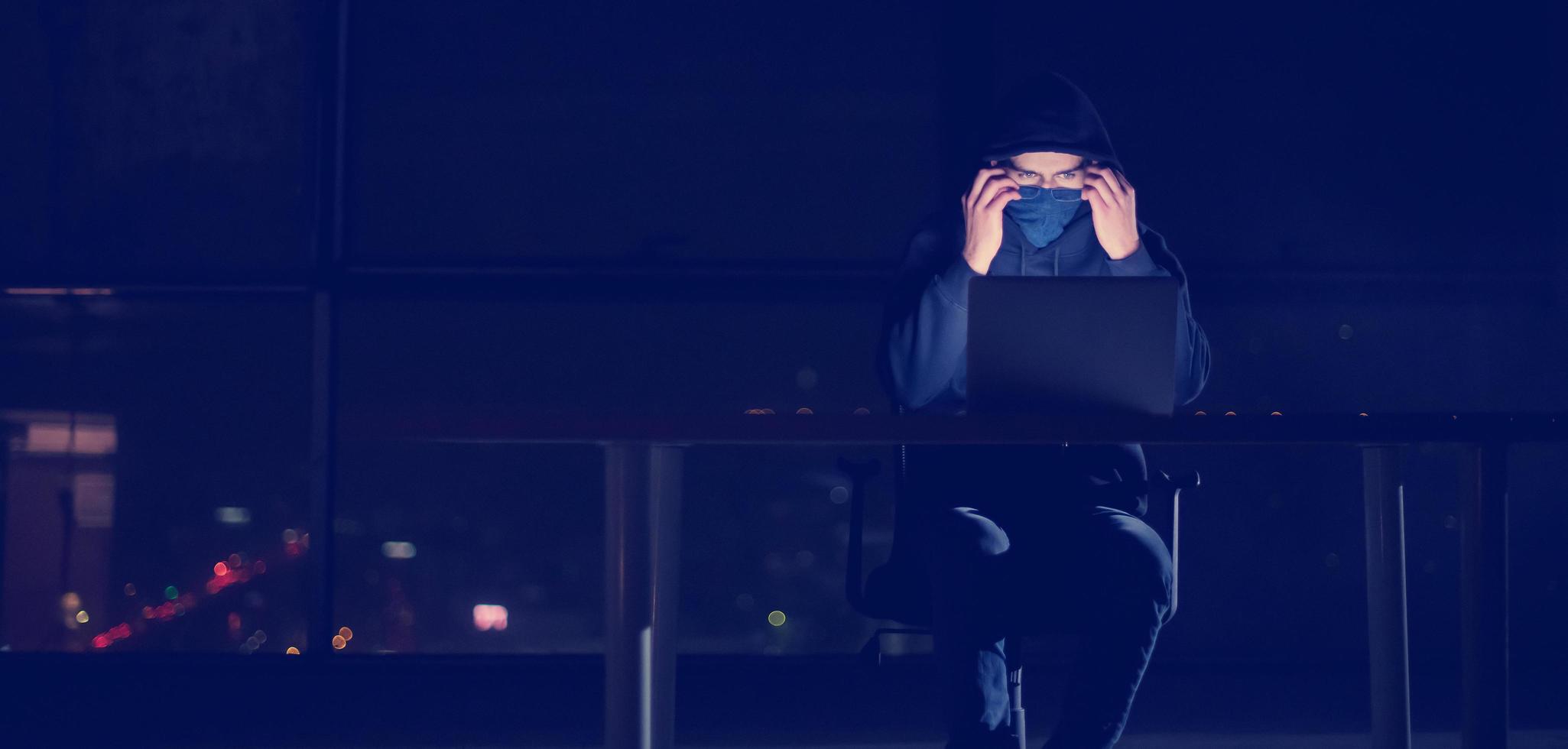 hacker using laptop computer while working in dark office photo