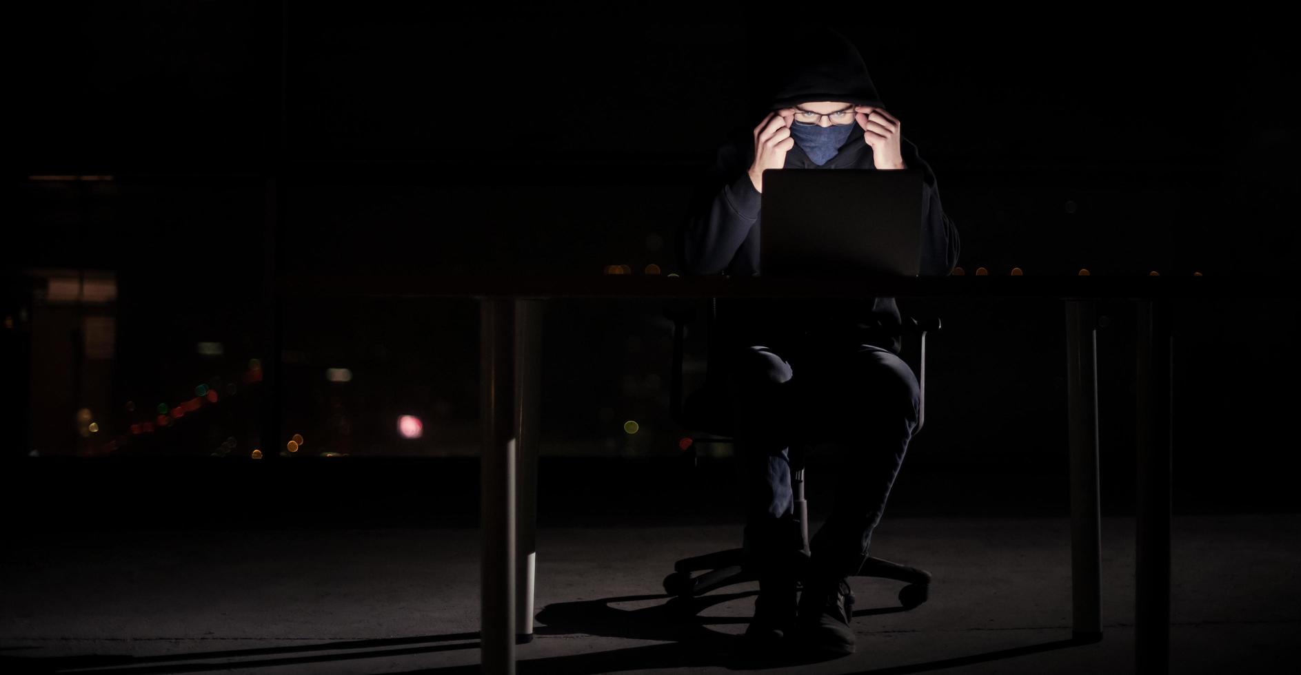 hacker using laptop computer while working in dark office photo