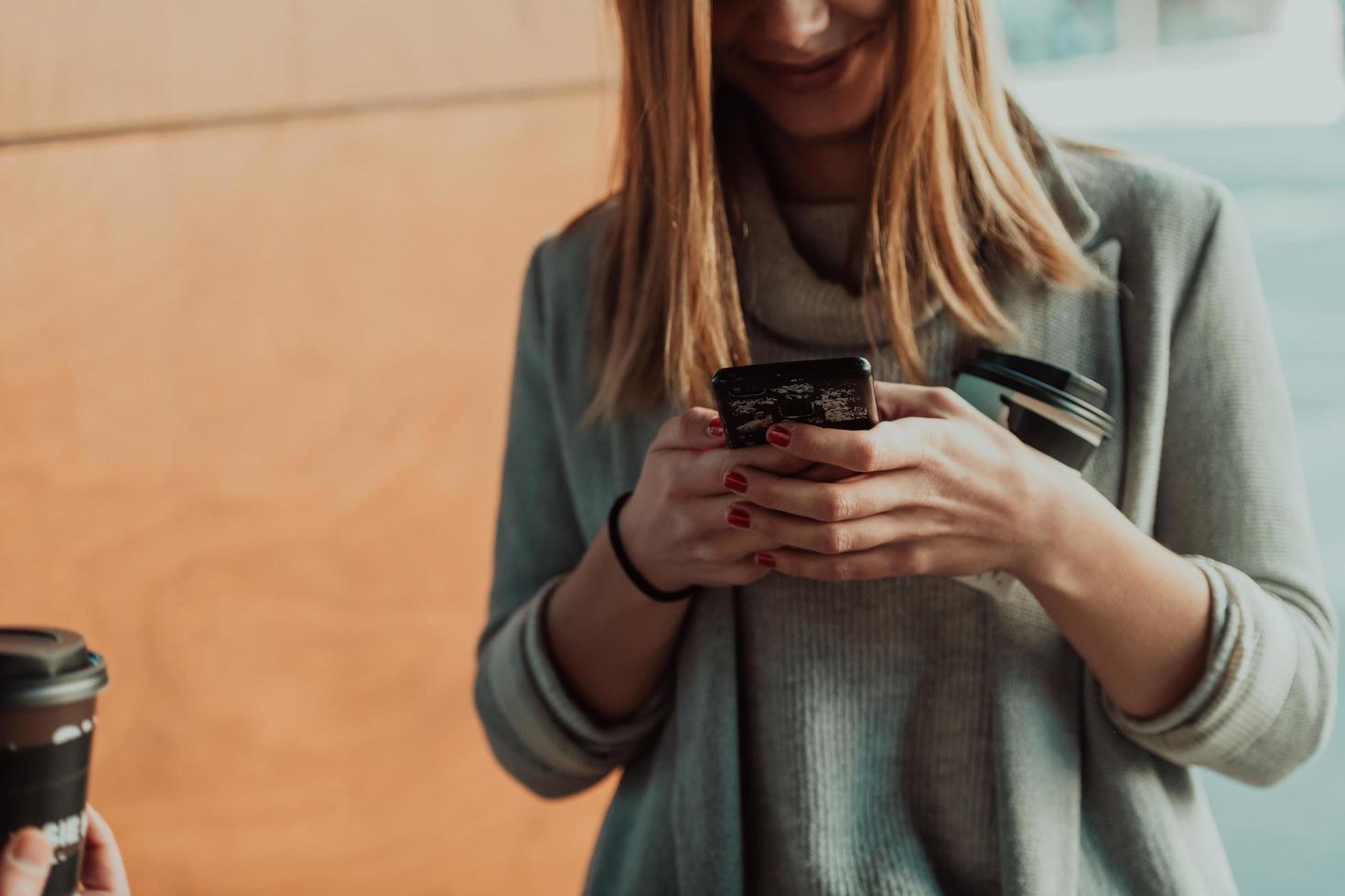 foto macro de una chica tomando café y usando un teléfono celular durante un descanso del trabajo.