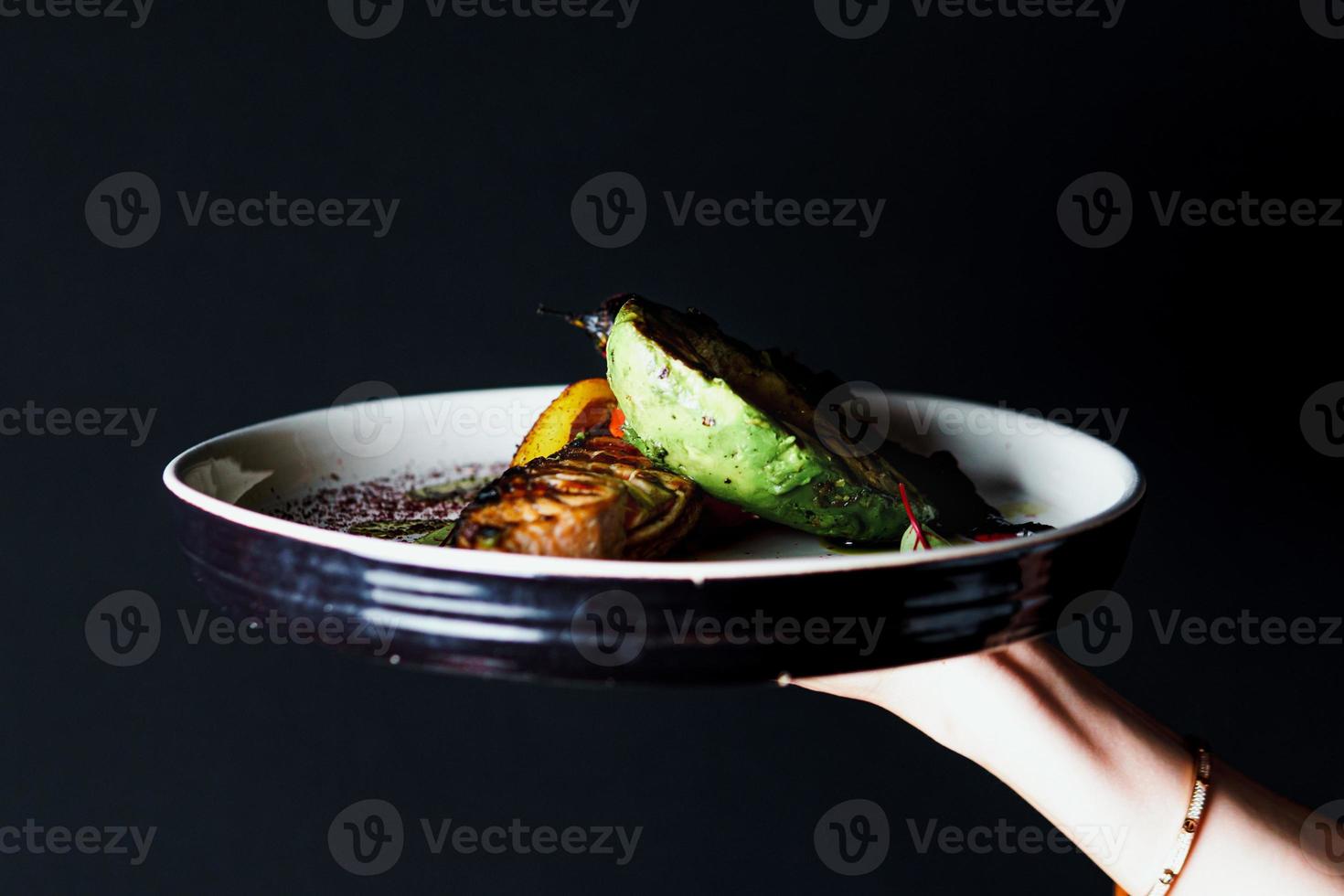 Grilled salmon fish fillet with vegetables and avocado on the plate, close up photo