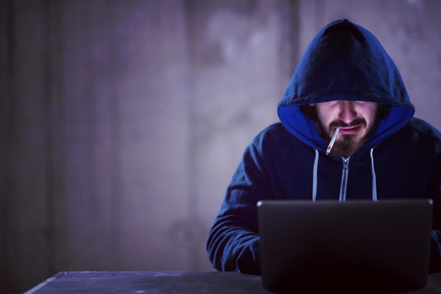 young hacker using laptop computer while working in dark office photo