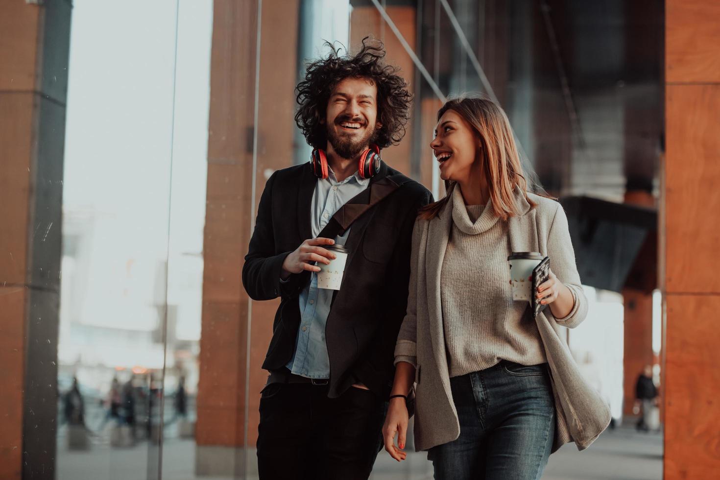 two people on a break from work walk in front of a modern company where they work and drink coffee. photo