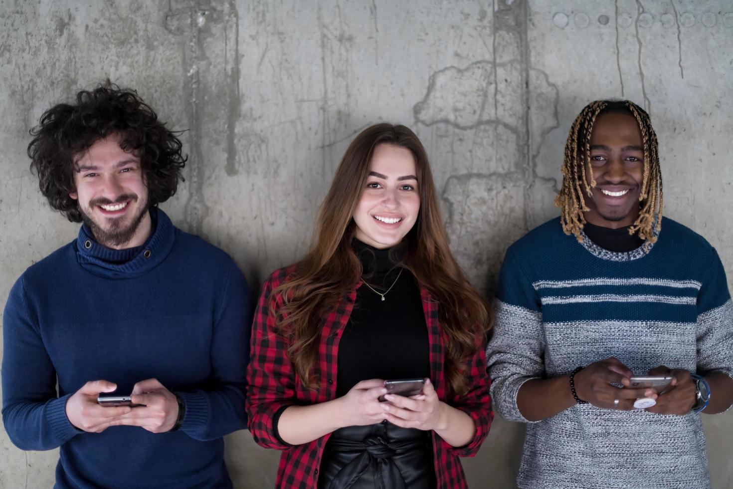 casual multiethnic business team using mobile phones in front of a concrete wall photo
