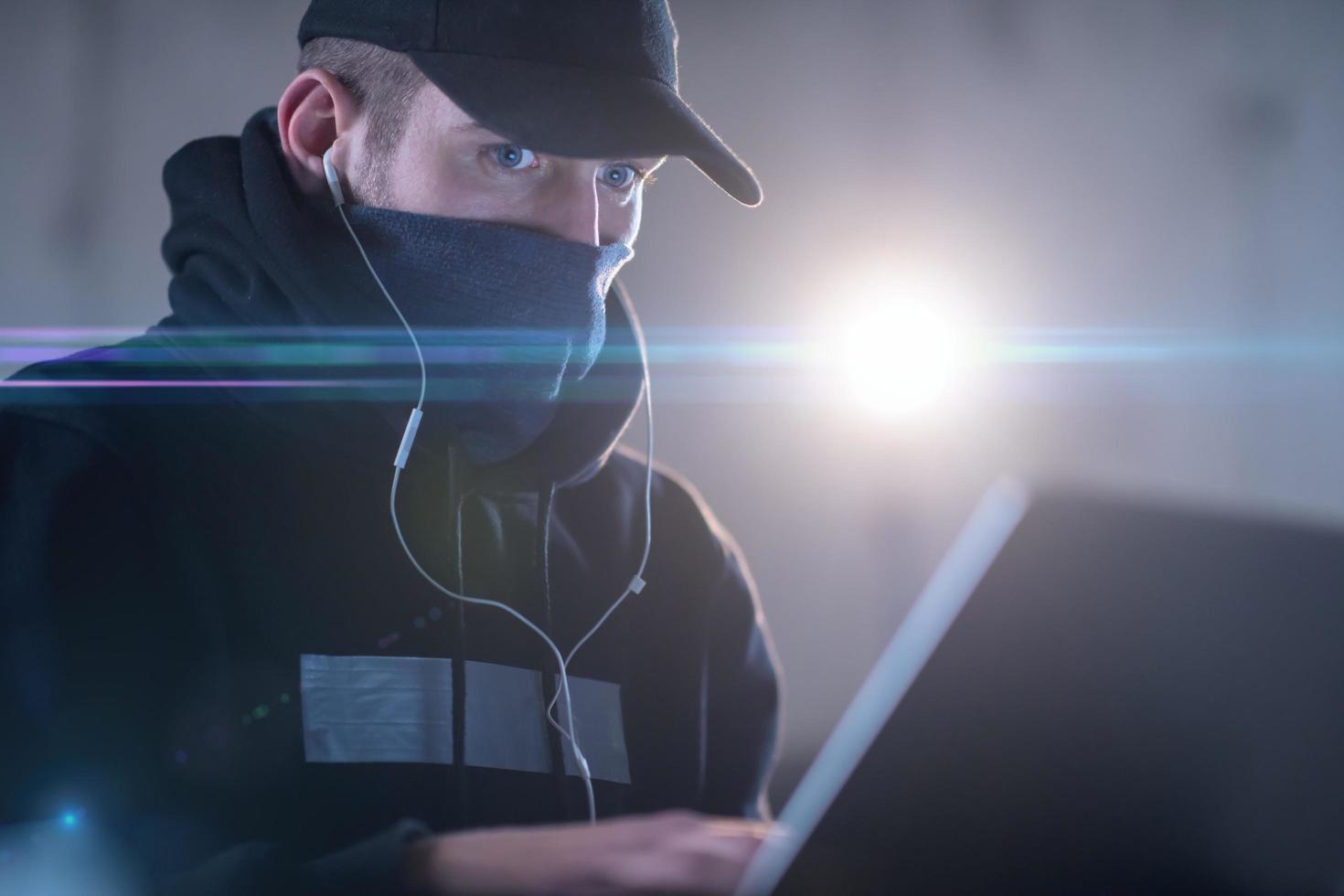 young talented hacker using laptop computer while working in dark office photo