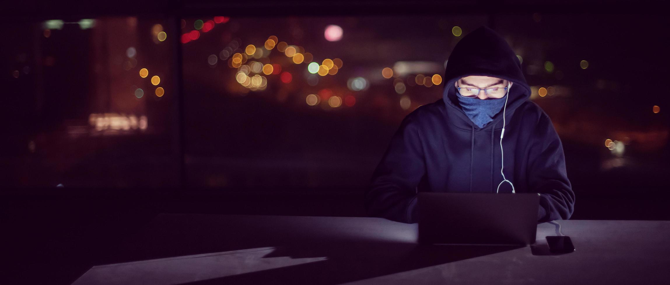 hacker using laptop computer while working in dark office photo