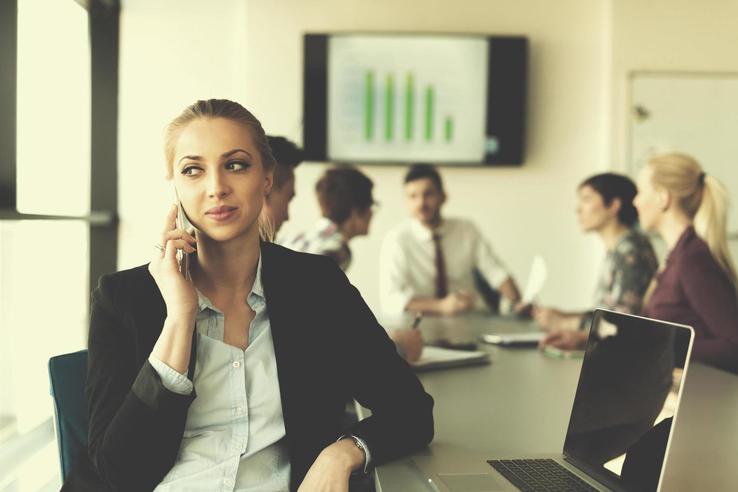 business woman speeking on phone at office with team on meeting in background photo