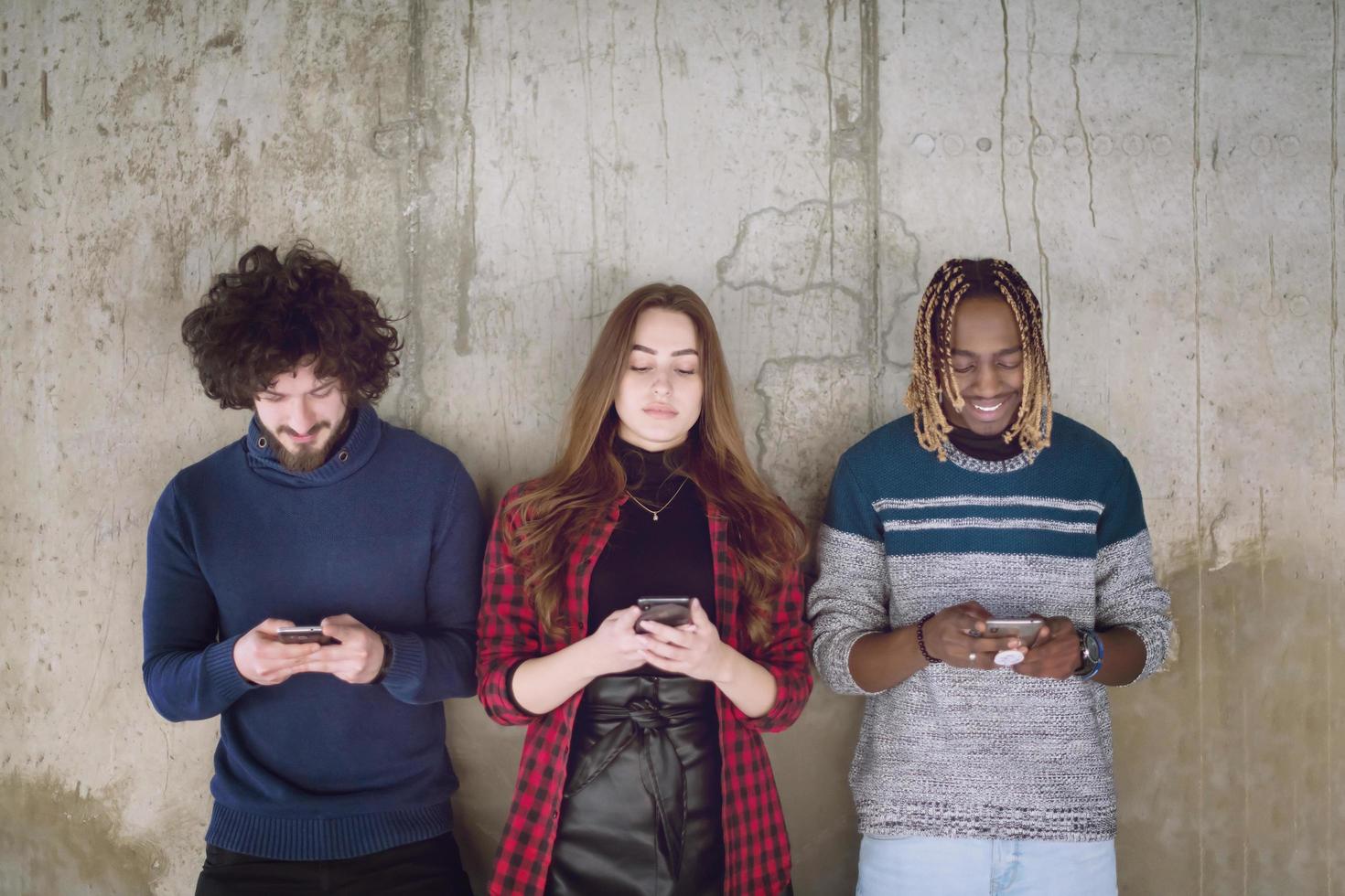 casual multiethnic business team using mobile phones in front of a concrete wall photo