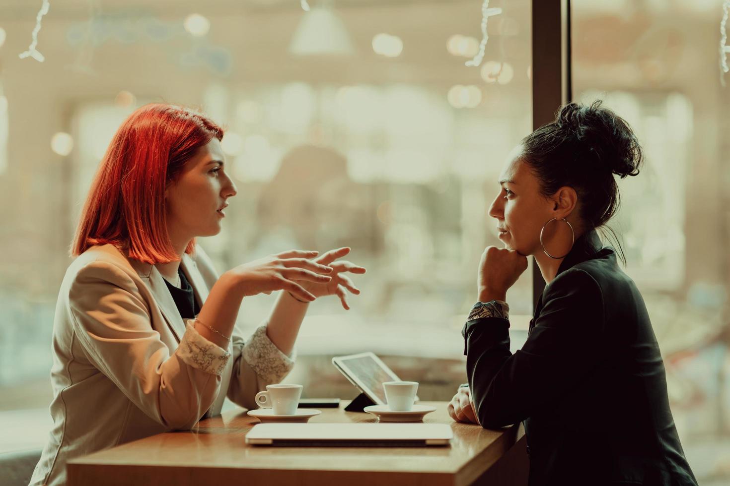Two young business women sitting at table in cafe.Girl using laptop, smartphone, blogging. Teamwork, business meeting. Freelancers working... photo