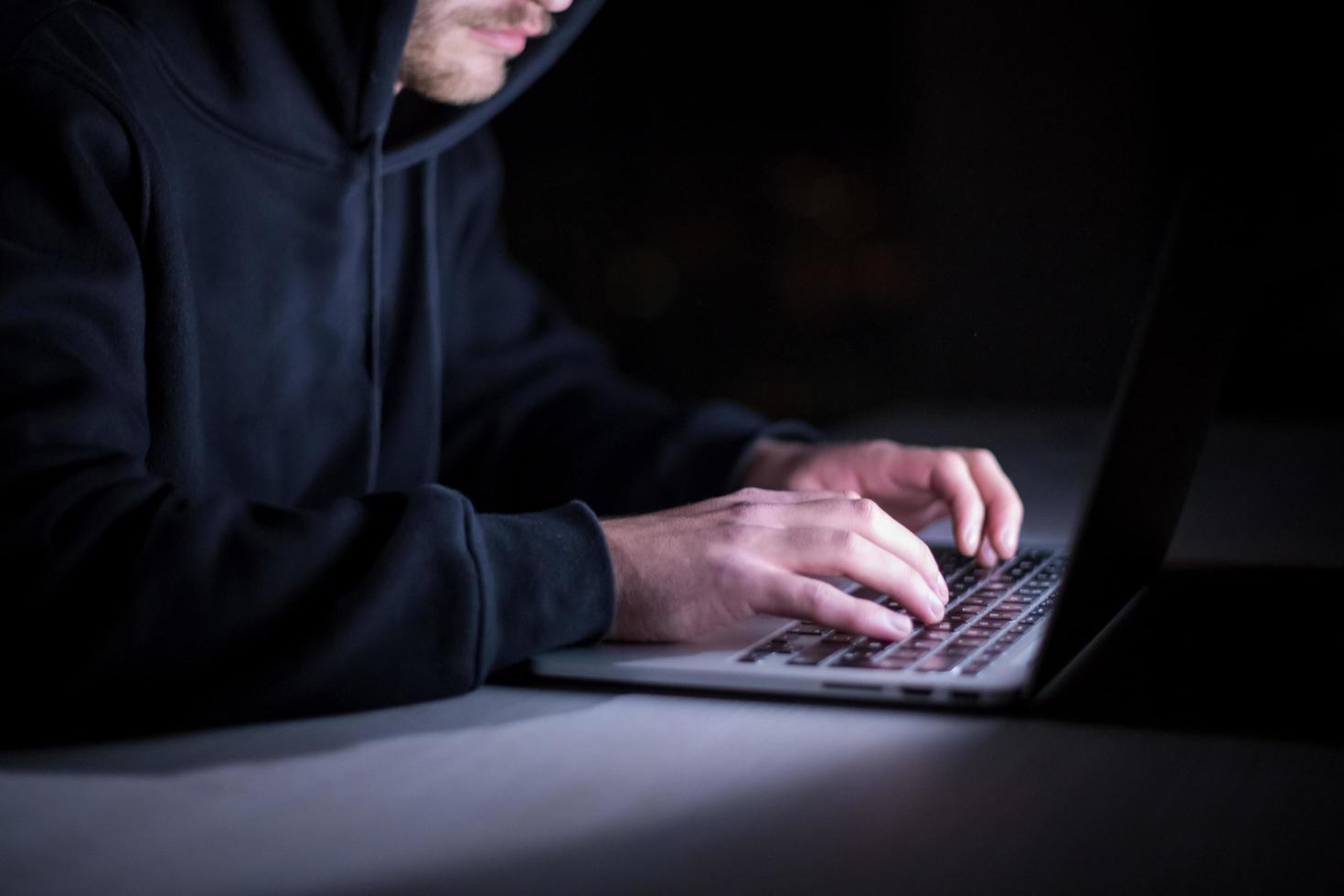 hacker using laptop computer while working in dark office photo
