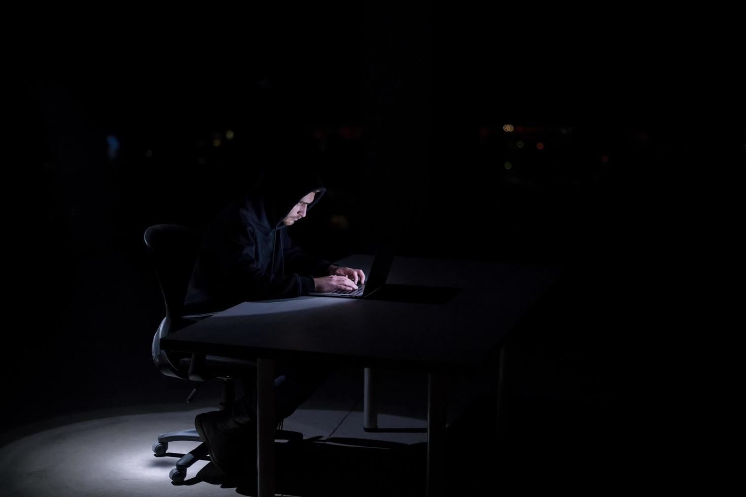 hacker using laptop computer while working in dark office photo