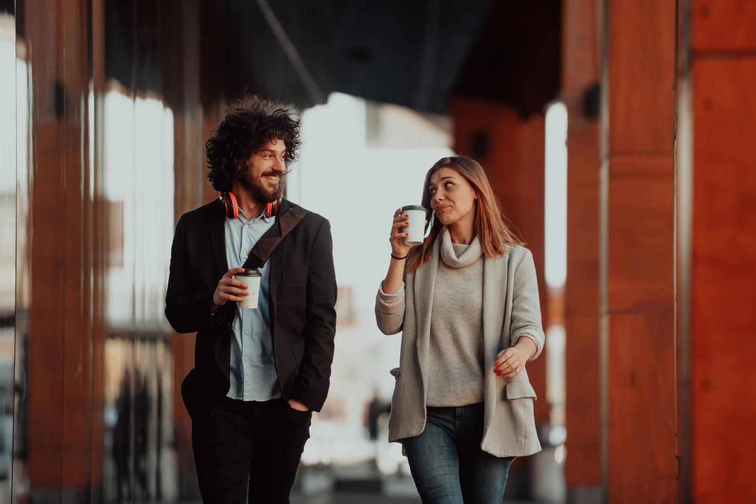 two young people on a break from work walk in front of a modern company where they work and drink coffee. photo