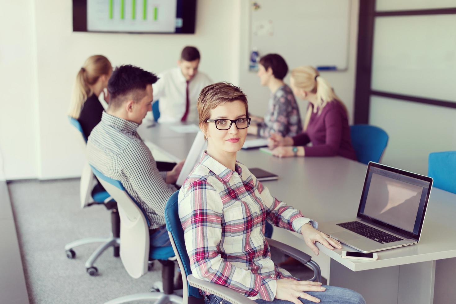 young business woman at office working on laptop with team on meeting in background photo