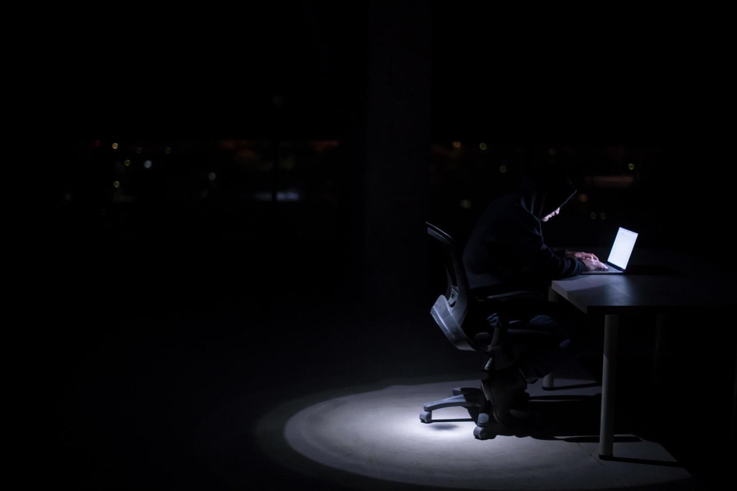 hacker using laptop computer while working in dark office photo