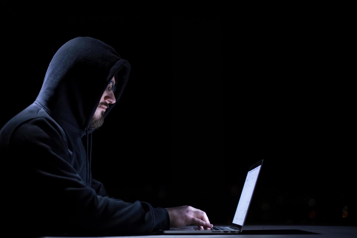 hacker using laptop computer while working in dark office photo
