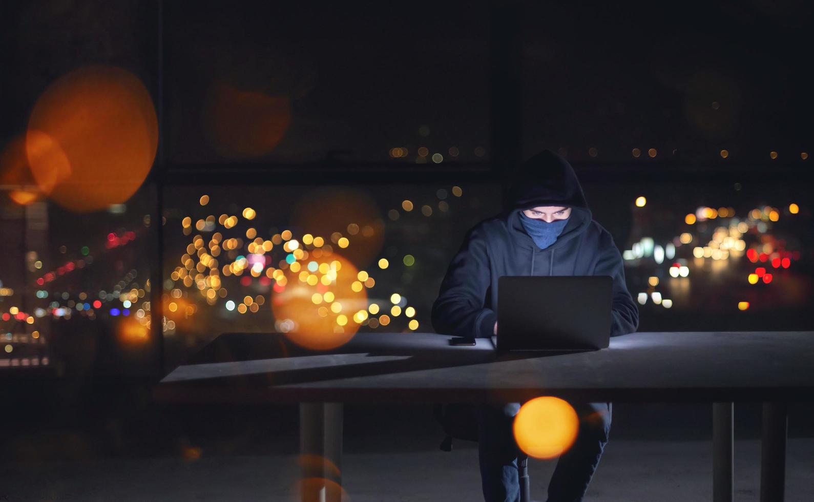 hacker using laptop computer while working in dark office photo