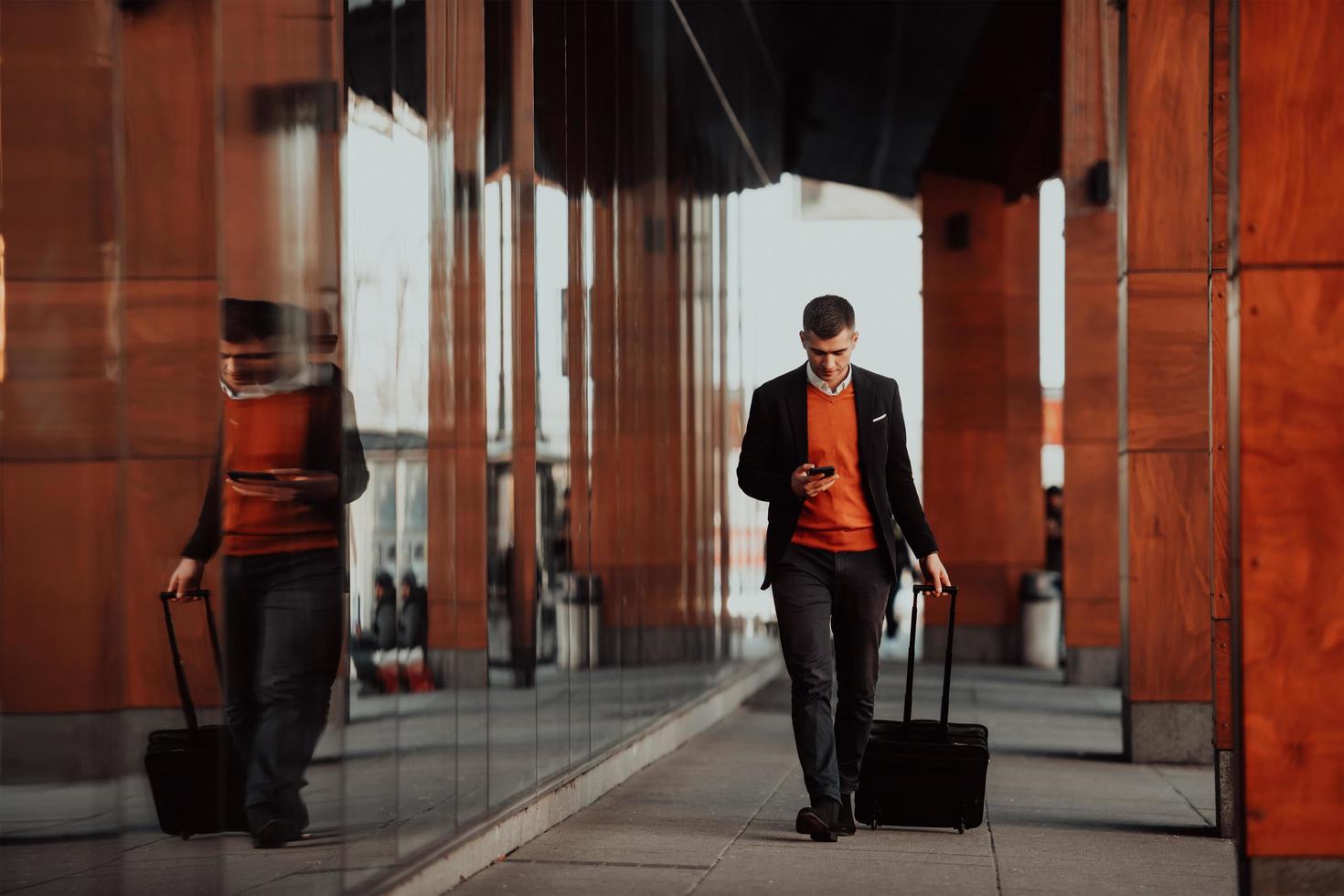 Going to airport terminal. Confident businessman traveler walking on city streets and pulling his suitcase drinking coffee and speaking on smartphone photo