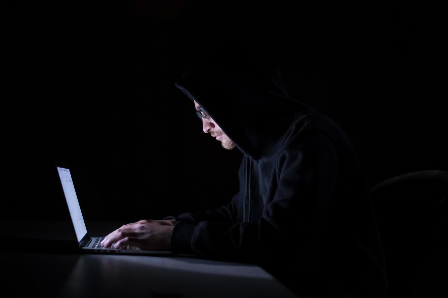 hacker using laptop computer while working in dark office photo