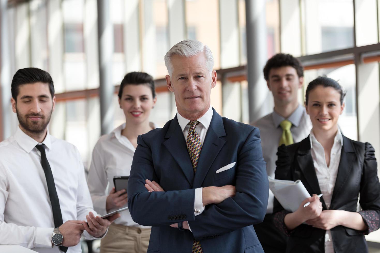 portrait of senior businessman as leader  with group of people in background as team photo