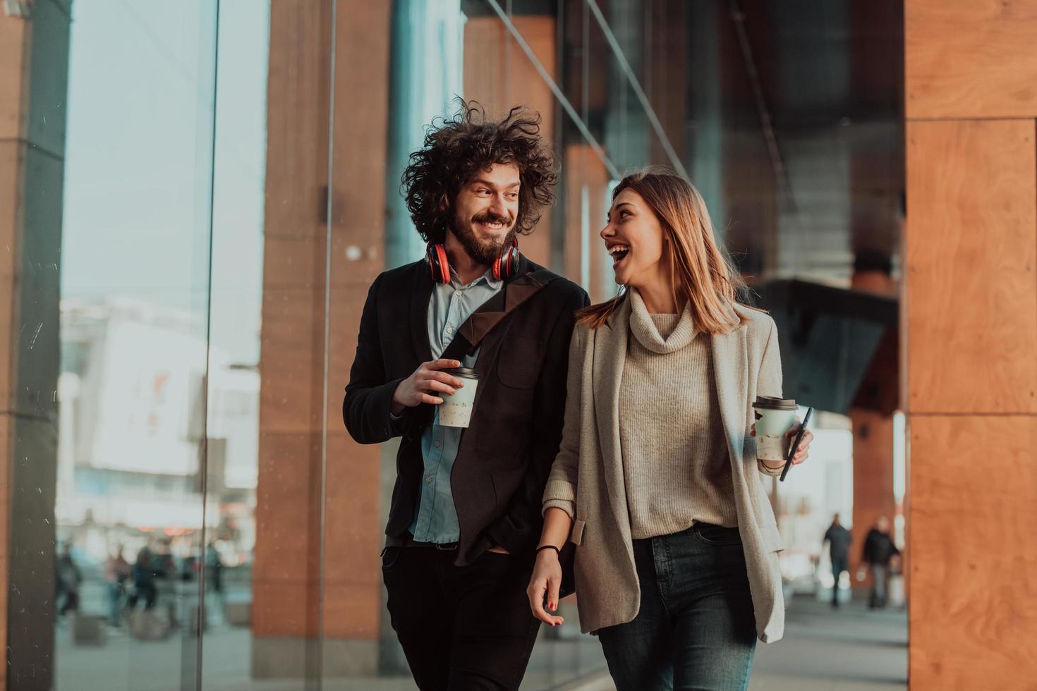 two people on a break from work walk in front of a modern company where they work and drink coffee. photo