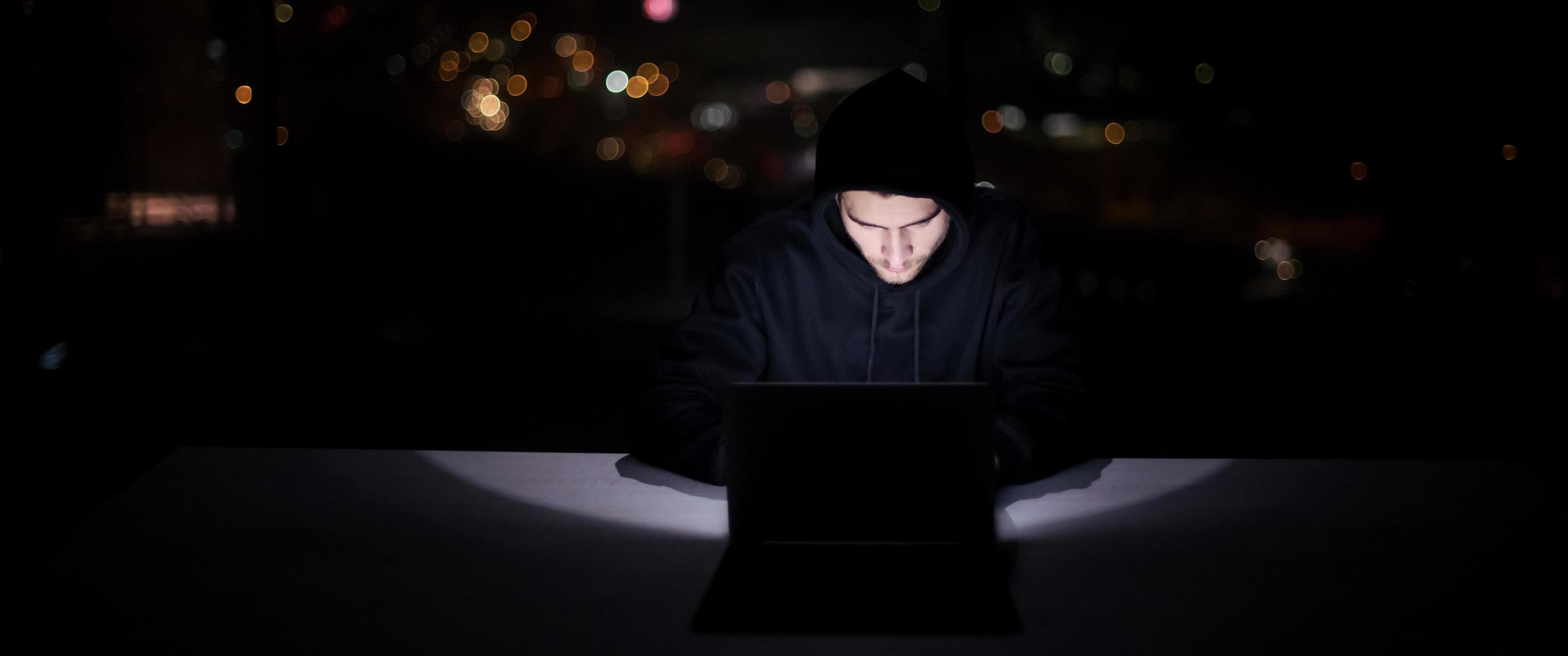 hacker using laptop computer while working in dark office photo