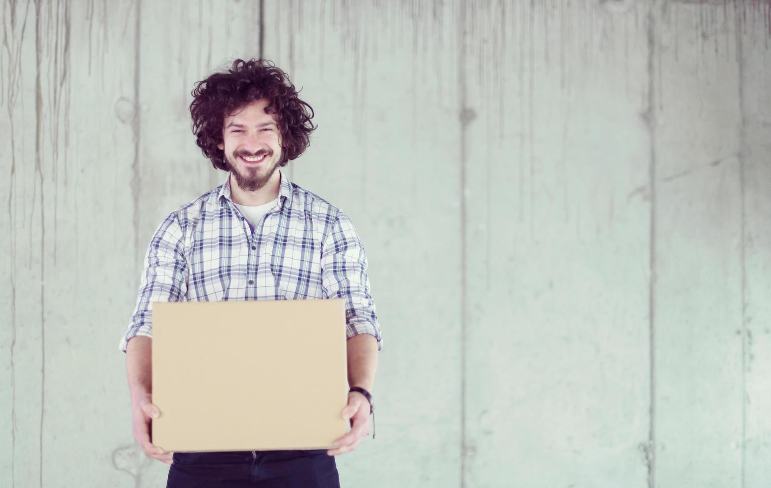 casual businessman carrying cardboard box in front of a concrete wall photo