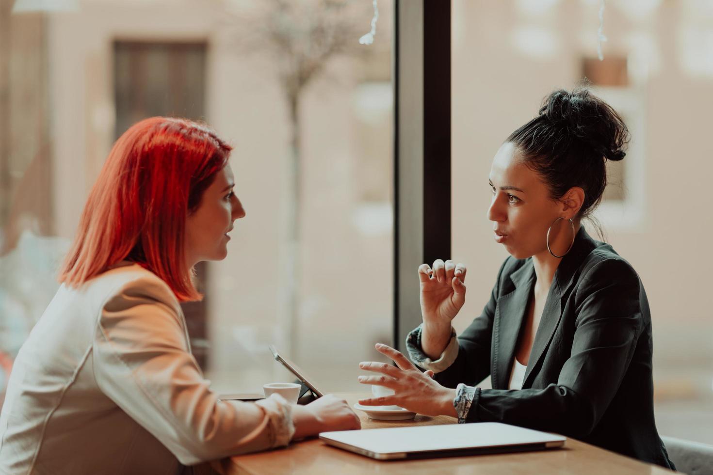 Two young business women sitting at table in cafe.Girl using laptop, smartphone, blogging. Teamwork, business meeting. Freelancers working... photo