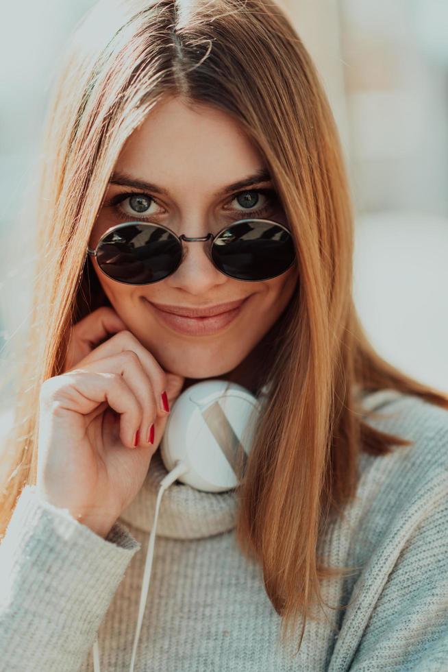 a modern girl with sunglasses walking down the street listens to music in headphones. photo
