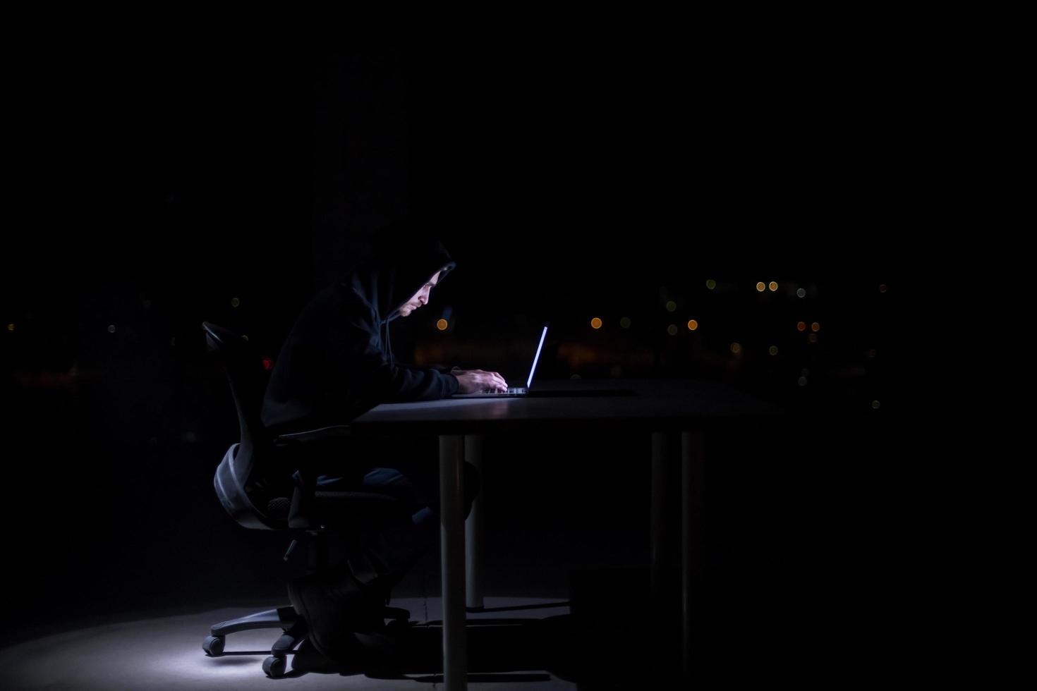 hacker using laptop computer while working in dark office photo