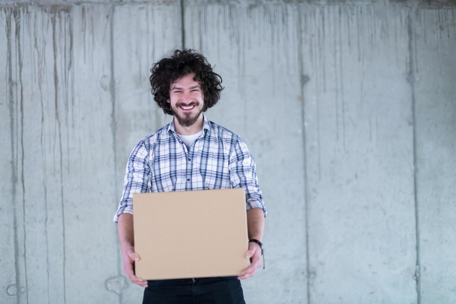 casual businessman carrying cardboard box in front of a concrete wall photo