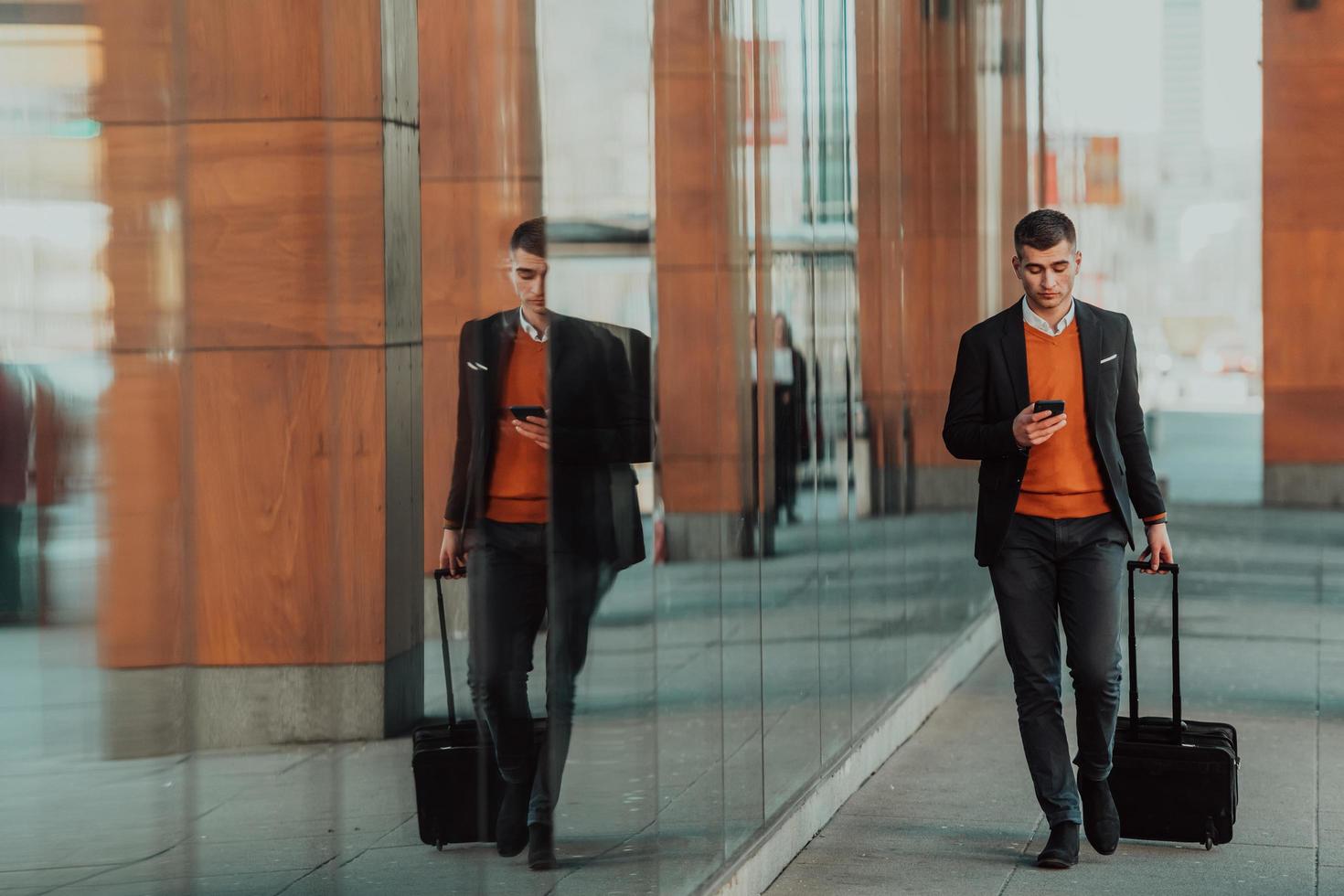 Going to airport terminal. Confident businessman traveler walking on city streets and pulling his suitcase drinking coffee and speaking on smartphone photo