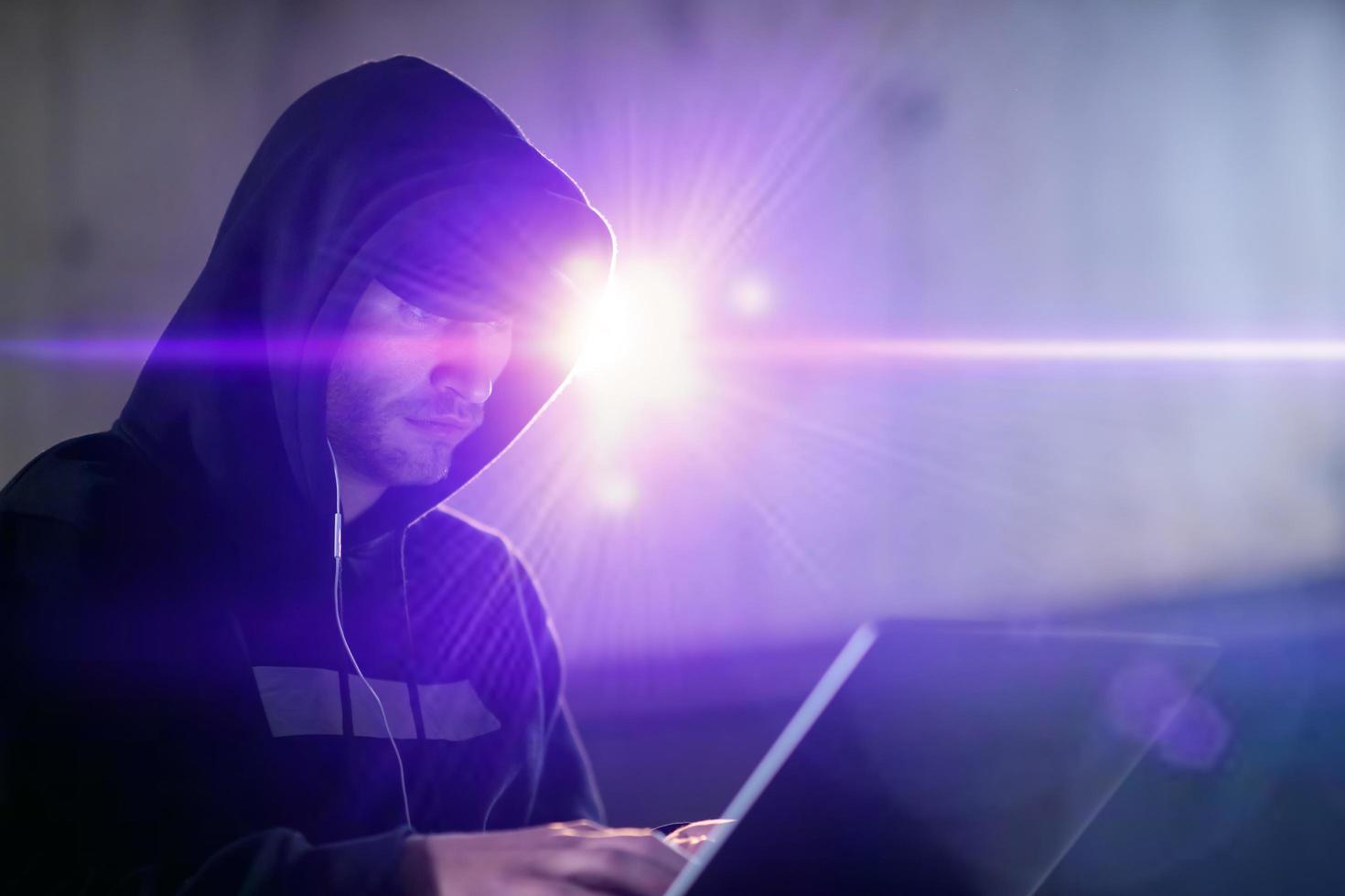 young talented hacker using laptop computer while working in dark office photo