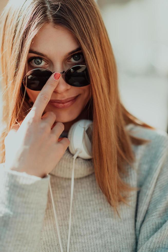 a modern girl with sunglasses walking down the street listens to music in headphones. photo