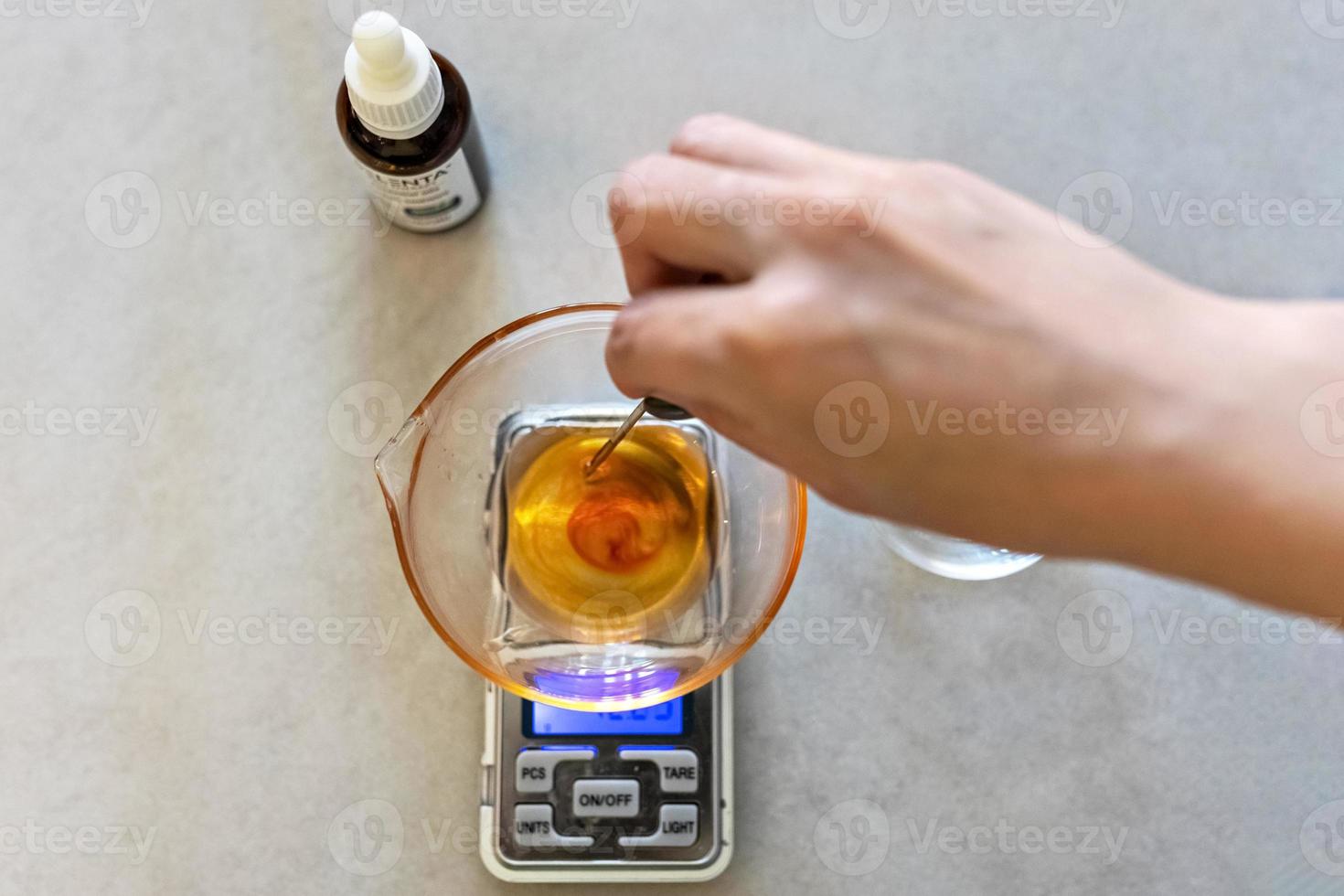 A soap-maker woman weighs aromatic oils for making cosmetics on a kitchen scale. Home spa. Small business photo