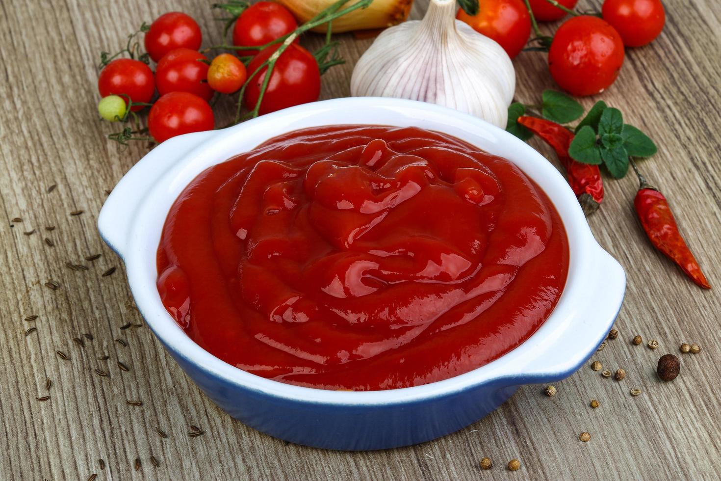 ketchup de tomate en un recipiente sobre fondo de madera foto