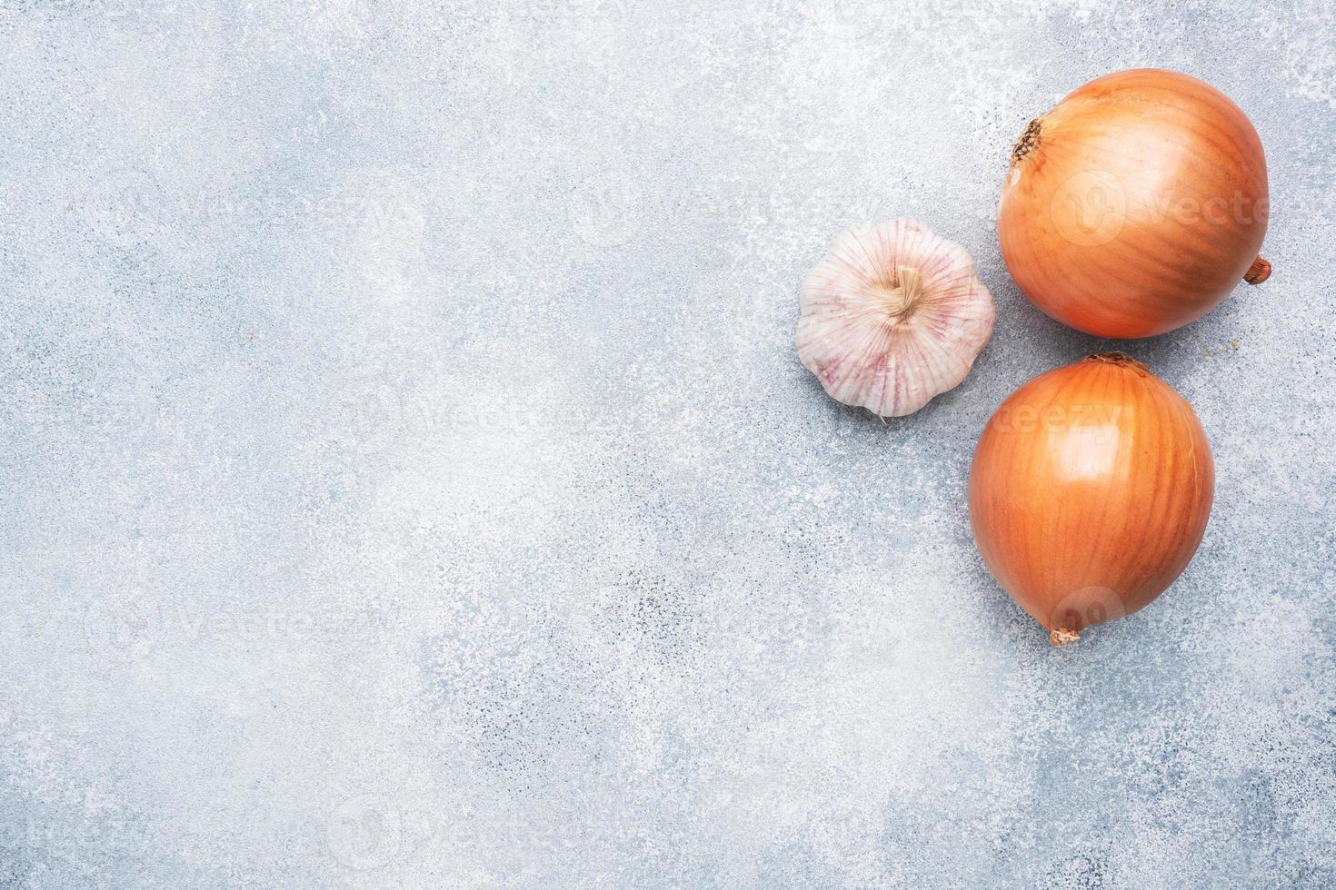 Two raw onions and a head of garlic on a concrete gray background with copy space. photo