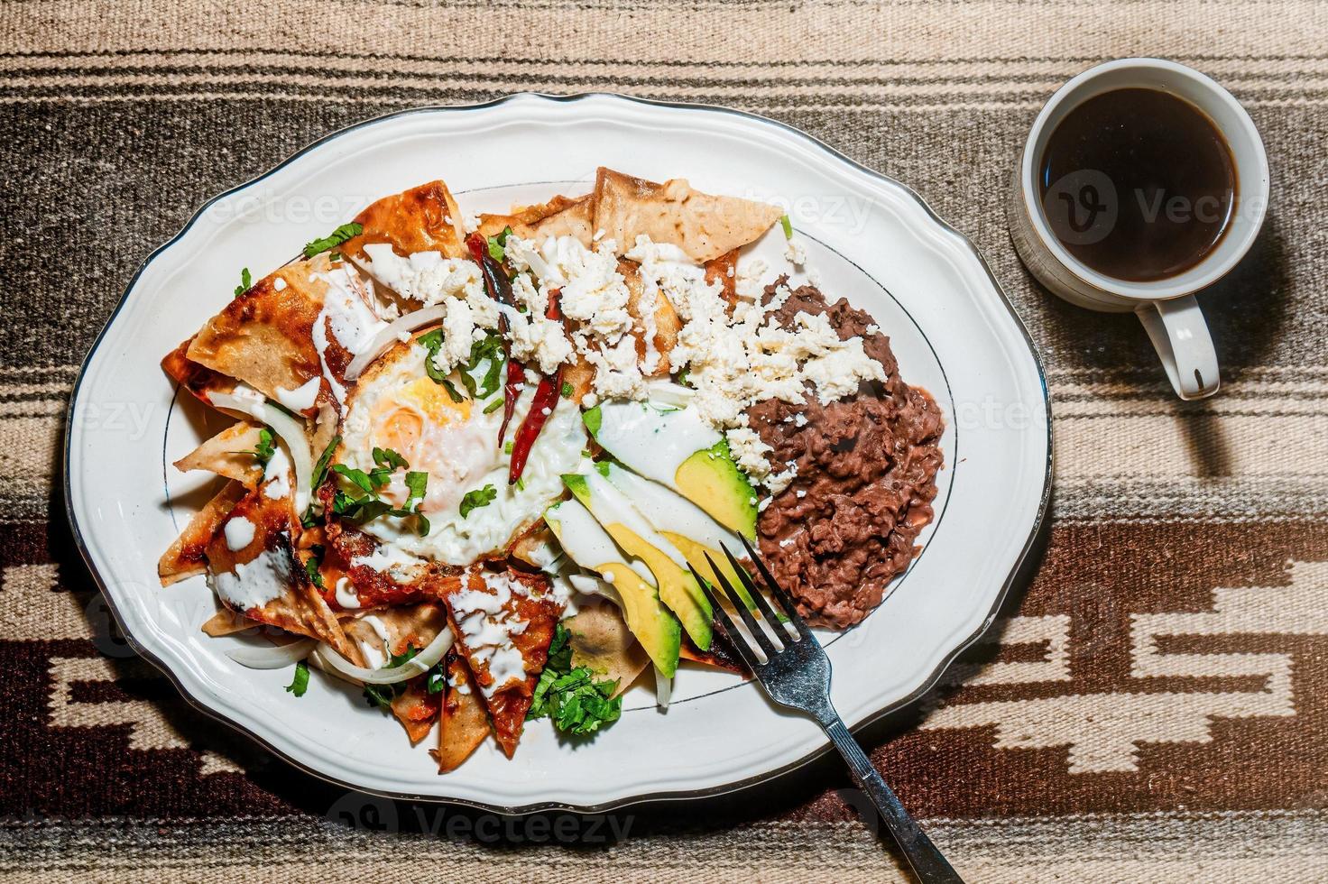 Chilaquiles Mexican food with in red sauce, cheese, cream, chili peppers on vintage background and coffee photo