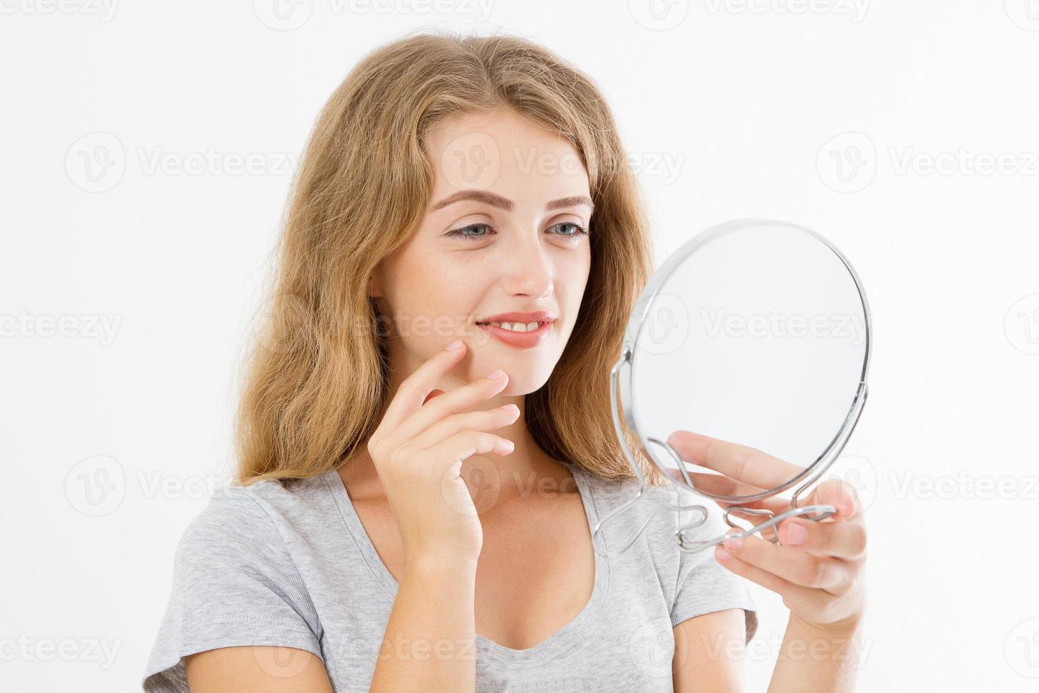 Young caucasian blonde woman looking wrinkles on face in mirror isolated on white background. Skin care and makeup concept. Copy space photo