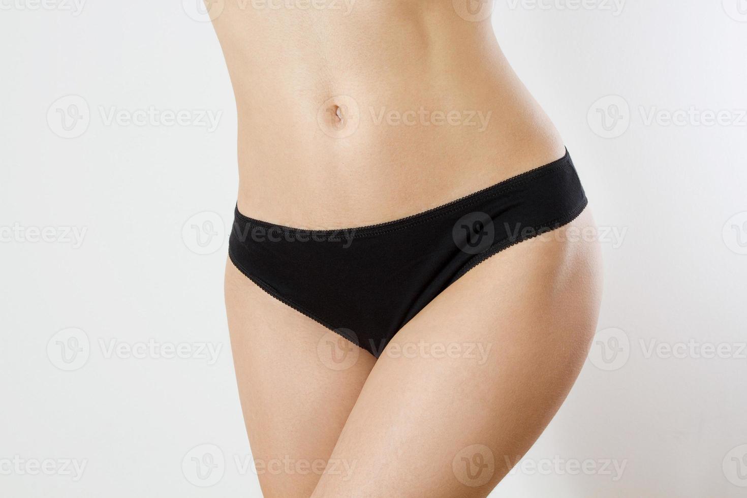 Healthy nutrition and belly health concept. Close up of woman flat stomach. Black Blank Template female panties with copy space and mock up. Front view. Cropped image, female bodycare isolated on gray photo