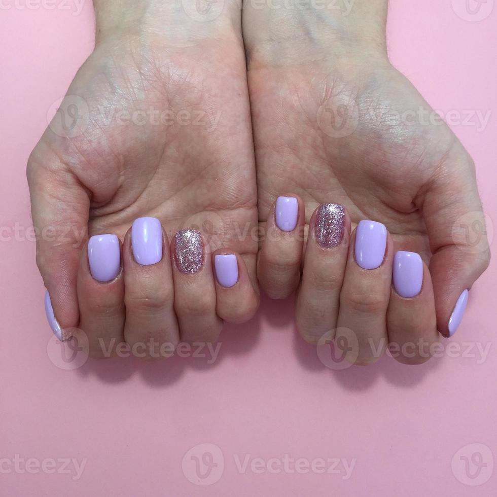 Manicure of different colors on nails. Female manicure on the hand on pink background photo