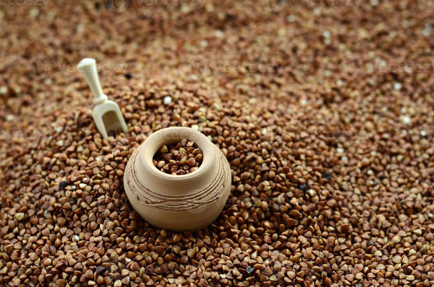 Background image of a large pile of buckwheat, in the middle of which lies a small jug and a wooden spatula for cereals photo