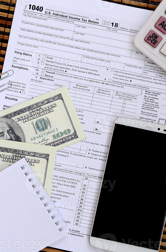 Composition of items lying on the 1040 tax form. Dollar bills, calculator, smartphone, paper clip and notepad. The time to pay taxes photo