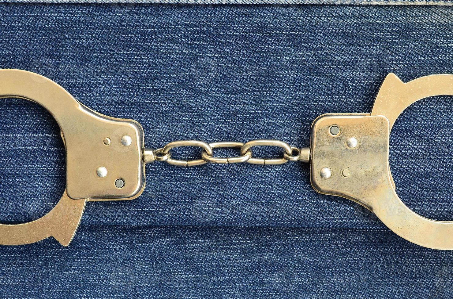 Police steel handcuffs lying on dark blue jeans background photo