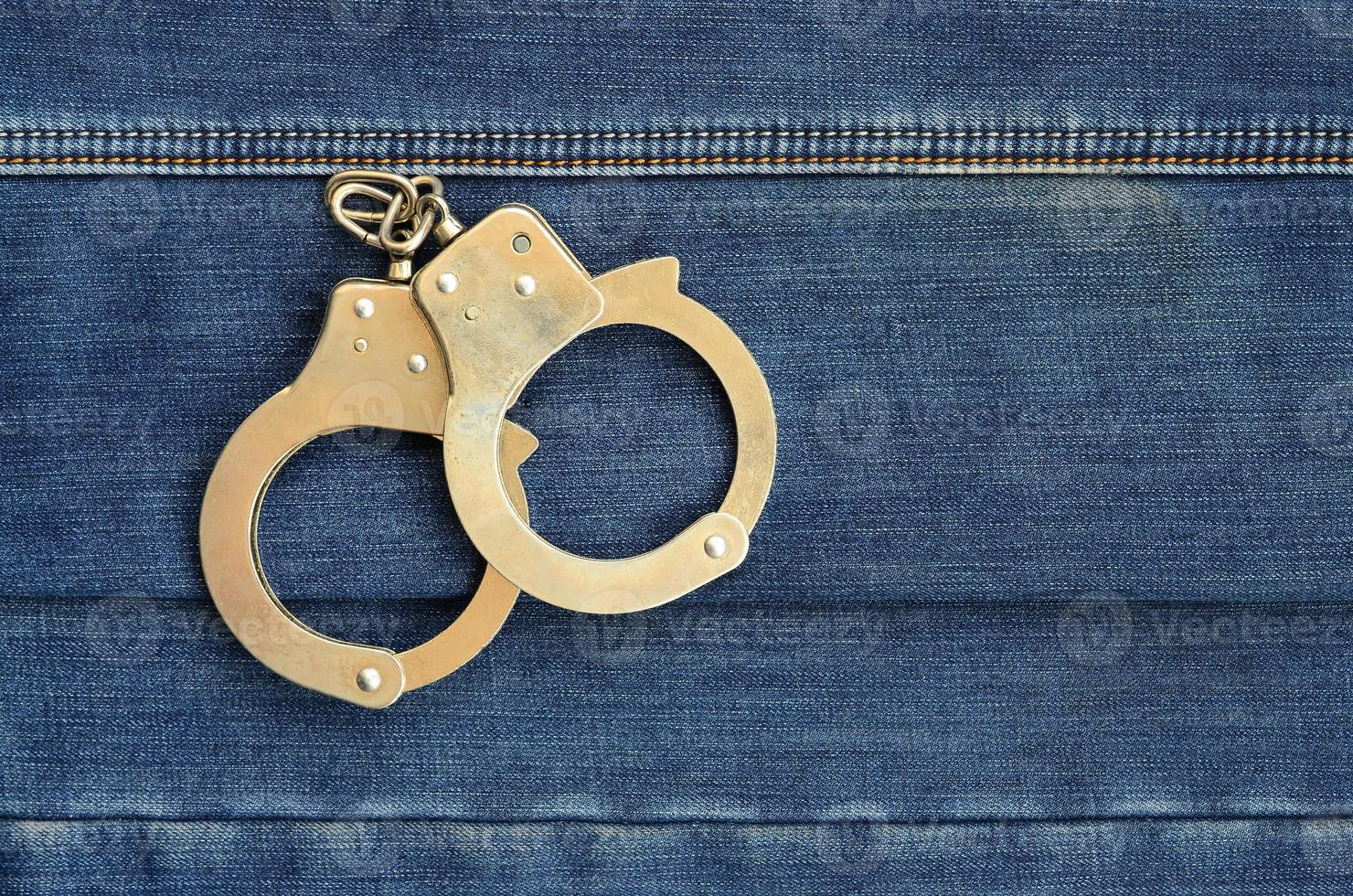 Police steel handcuffs lying on dark blue jeans background photo