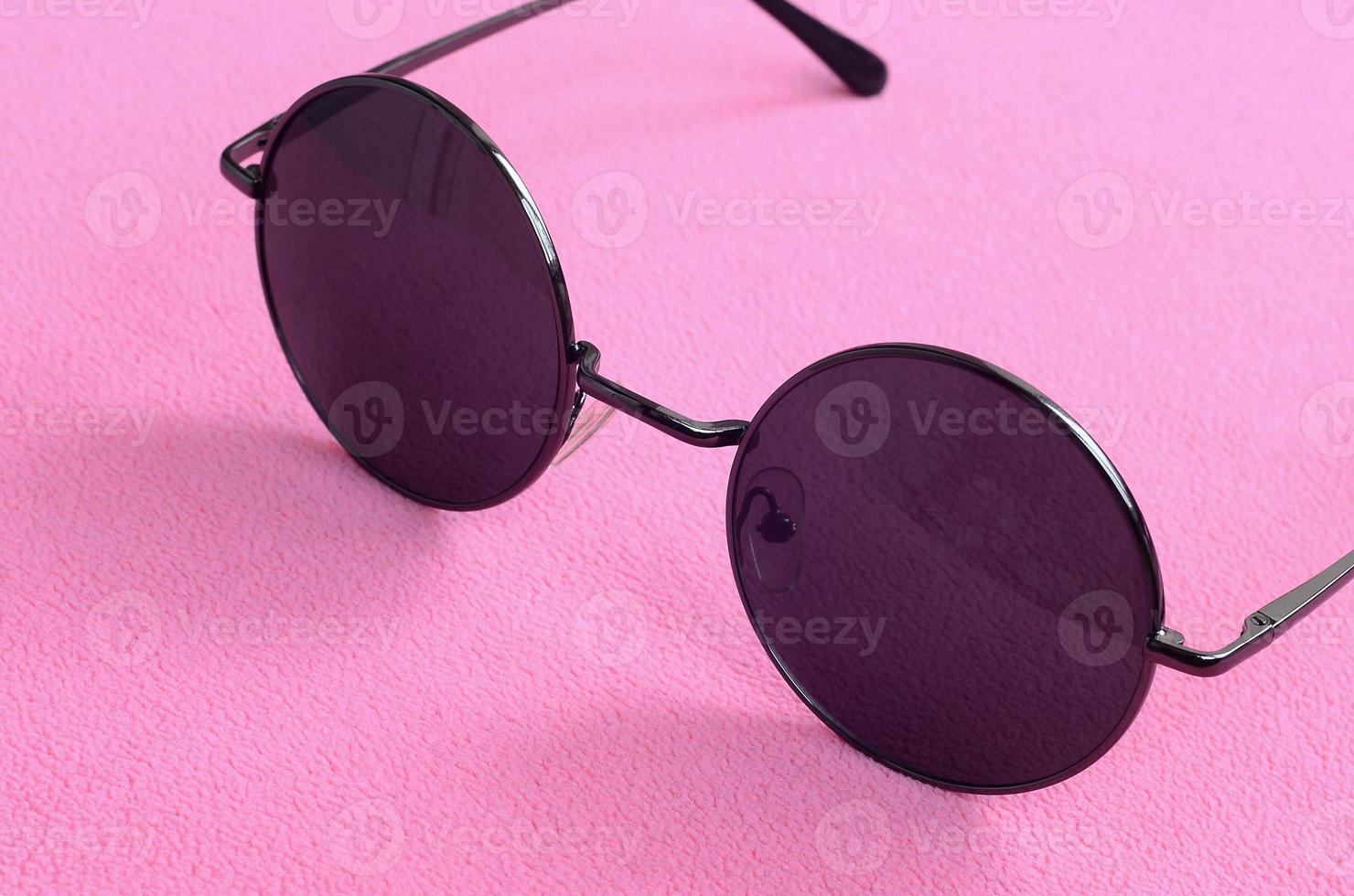 Stylish black sunglasses with round glasses lies on a blanket made of soft and fluffy light pink fleece fabric. Fashionable background picture in female colors photo