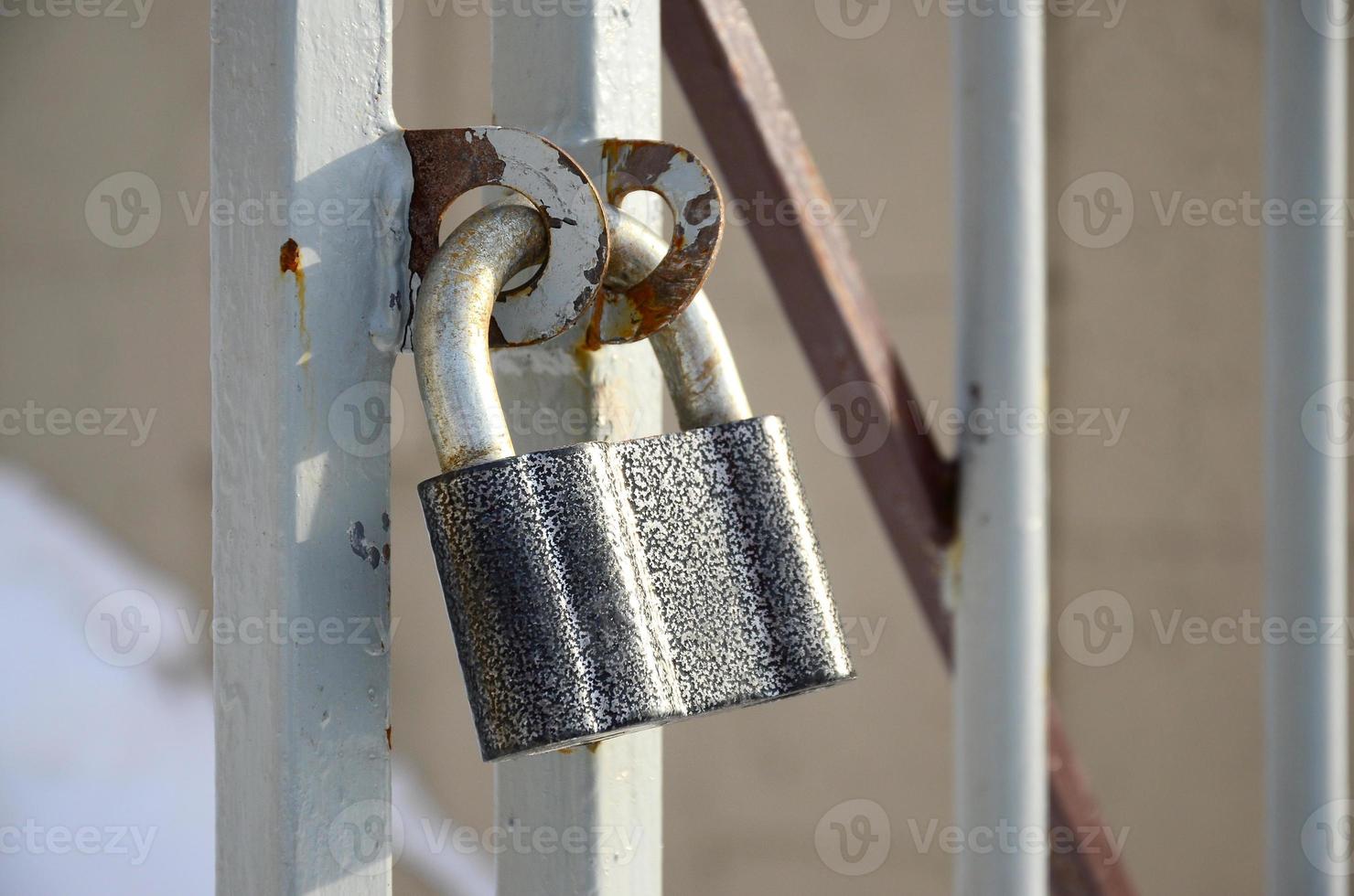 A large gray padlock hangs on a metal gate photo