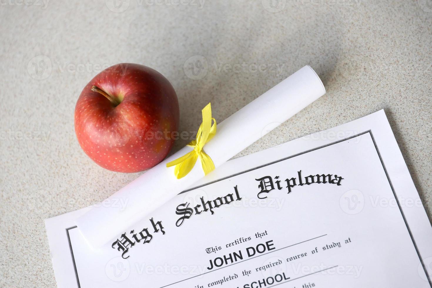 A high school diploma lies on table with small scroll and red apple. Education documents photo