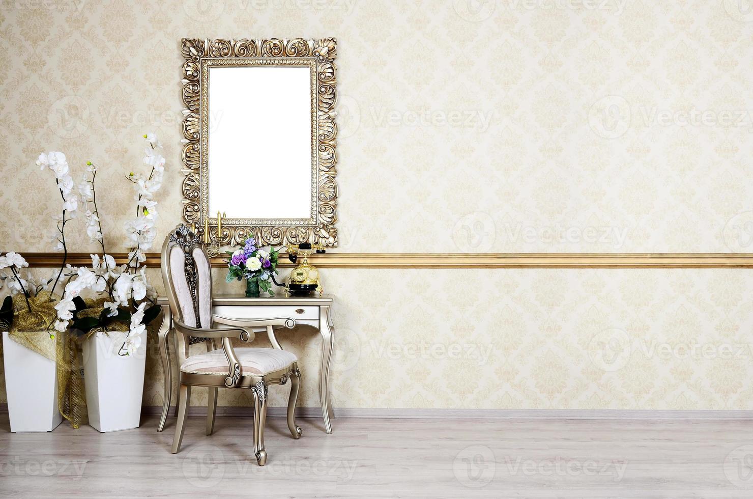 A fragment of a retro interior with a chair and table, on which is a telephone and a vase of flowers. Above the table hangs an empty picture frame for your photo